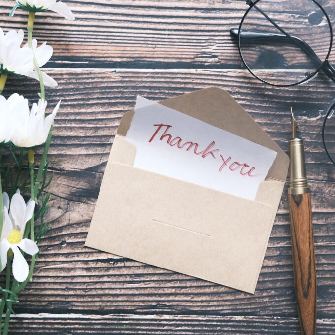 a thank you note sitting on top of a table next to a pair of glasses